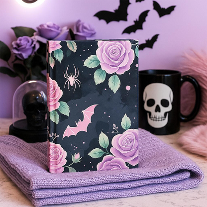 Notebook with floral design on a purple blanket, with a skull and bat mug in the background.